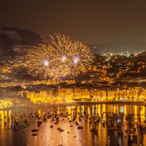 A breathtaking view of fireworks illuminating a vibrant city by the sea during the night.