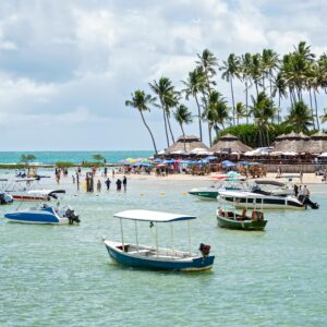 Scenic tropical beach with boats, palm trees, and crowds enjoying a sunny day.